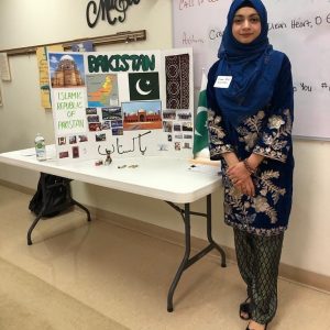 Photo of Kiran Bibi (Global UGRAD IREX), standing beside an informational poster about Pakistan.