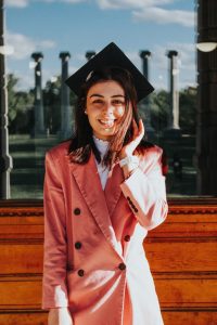 Photograph of Daina Fidarova standing in front of the MU columns, wearing a graduation cap.