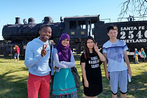 Four student pose for the camera in front of an old steam engine